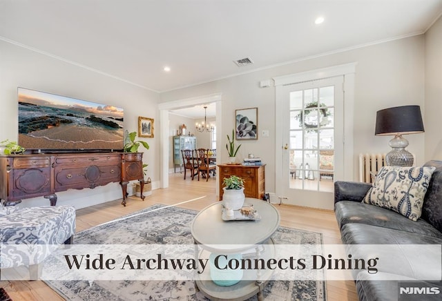 living room featuring hardwood / wood-style floors, crown molding, radiator, and a chandelier