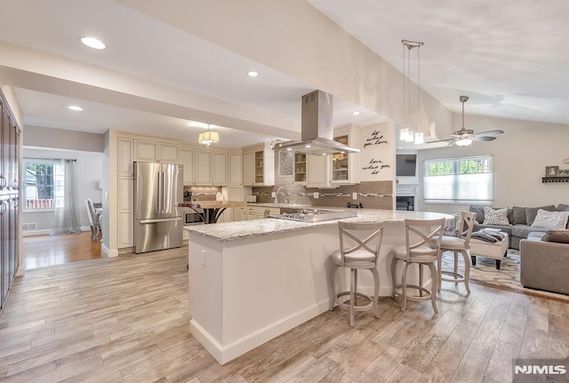 kitchen featuring light stone countertops, appliances with stainless steel finishes, island exhaust hood, decorative backsplash, and kitchen peninsula