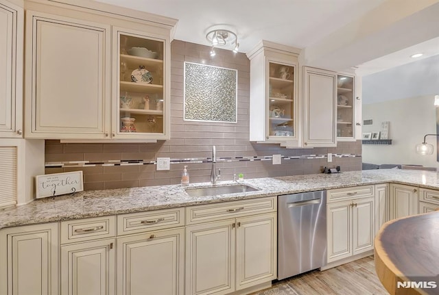 kitchen featuring light stone countertops, stainless steel dishwasher, cream cabinetry, light wood-type flooring, and sink