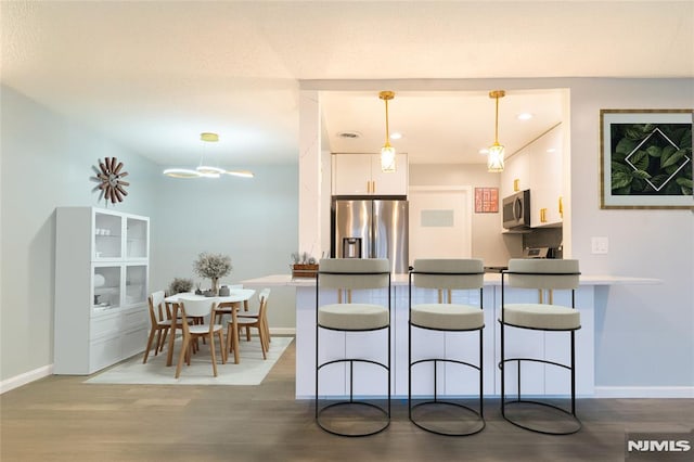 kitchen featuring kitchen peninsula, stainless steel appliances, decorative light fixtures, white cabinets, and a breakfast bar area