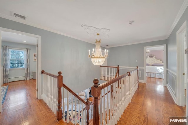 hallway featuring baseboard heating, light hardwood / wood-style floors, ornamental molding, and an inviting chandelier