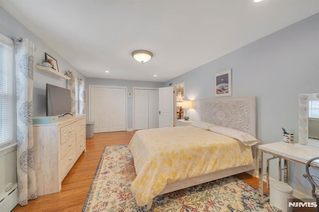 bedroom featuring a baseboard radiator, two closets, and light hardwood / wood-style floors