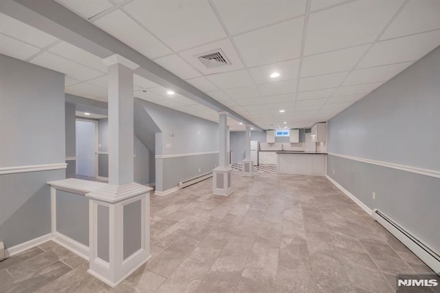 basement with a paneled ceiling and baseboard heating