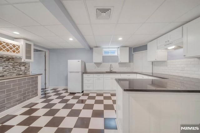 kitchen featuring backsplash, white refrigerator, sink, kitchen peninsula, and white cabinetry