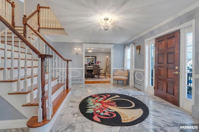 foyer with a chandelier, a baseboard heating unit, and ornamental molding