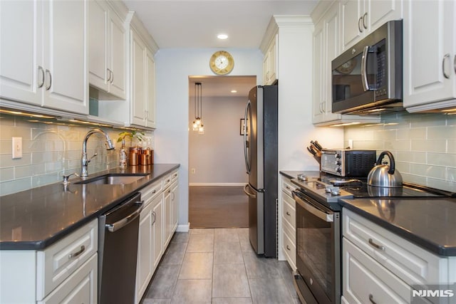 kitchen with hanging light fixtures, dark tile patterned flooring, white cabinets, appliances with stainless steel finishes, and sink