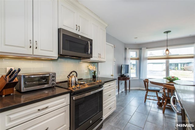 kitchen with stainless steel appliances, hanging light fixtures, dark tile patterned flooring, white cabinets, and backsplash