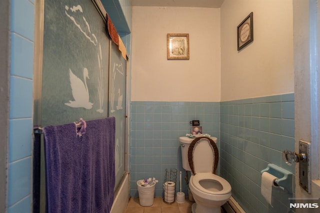 bathroom with tile patterned floors, bath / shower combo with glass door, a baseboard radiator, tile walls, and toilet