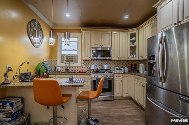 kitchen with light stone countertops, cream cabinets, pendant lighting, a kitchen bar, and appliances with stainless steel finishes