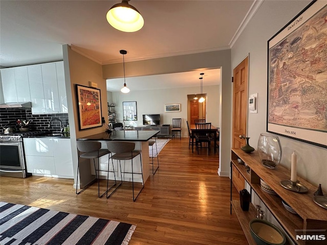 kitchen featuring a breakfast bar, kitchen peninsula, decorative backsplash, gas stove, and white cabinetry