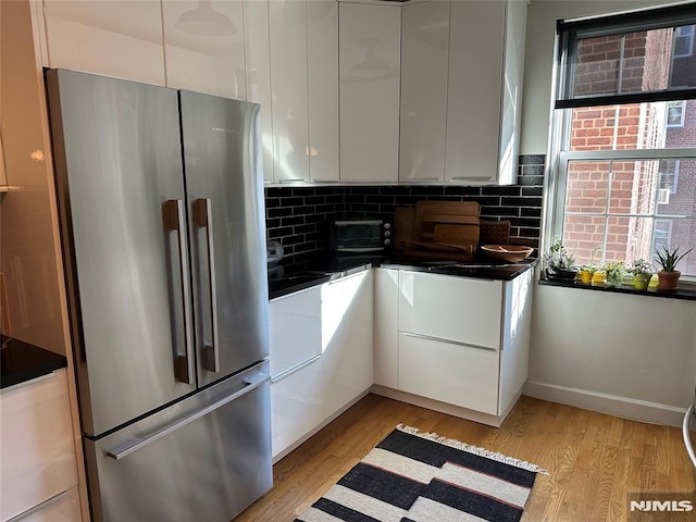 kitchen featuring white cabinets, stainless steel fridge, backsplash, and light hardwood / wood-style flooring