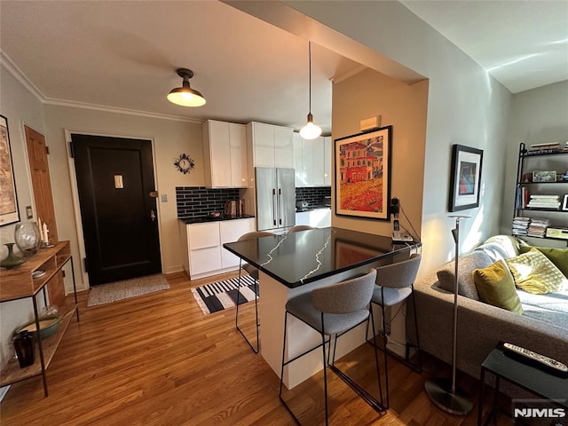 kitchen featuring backsplash, kitchen peninsula, light wood-type flooring, white cabinetry, and a breakfast bar area