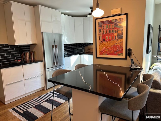 kitchen with stainless steel refrigerator, white cabinetry, tasteful backsplash, a kitchen breakfast bar, and decorative light fixtures