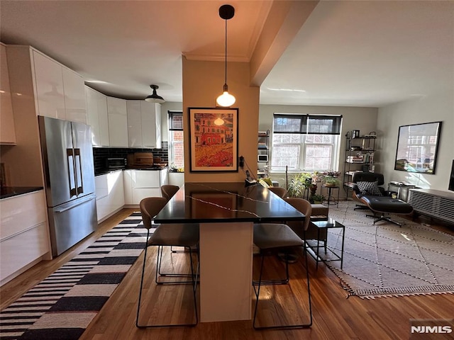 kitchen with a kitchen breakfast bar, stainless steel fridge, white cabinetry, and pendant lighting