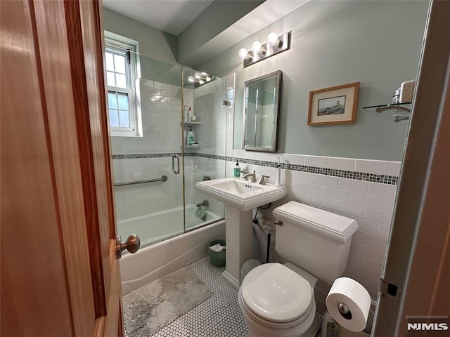 bathroom featuring tile patterned floors, combined bath / shower with glass door, toilet, and tile walls