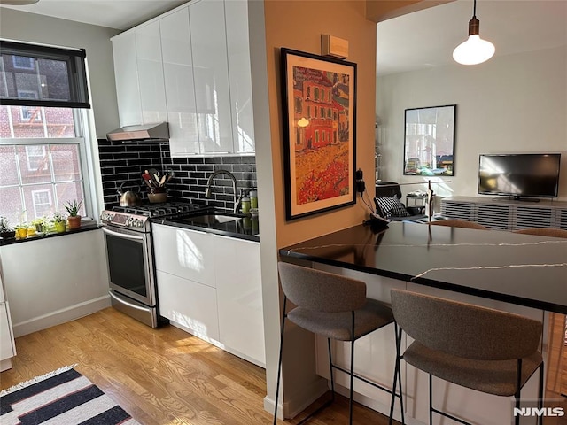 kitchen featuring light wood-type flooring, a breakfast bar, gas range, pendant lighting, and white cabinetry