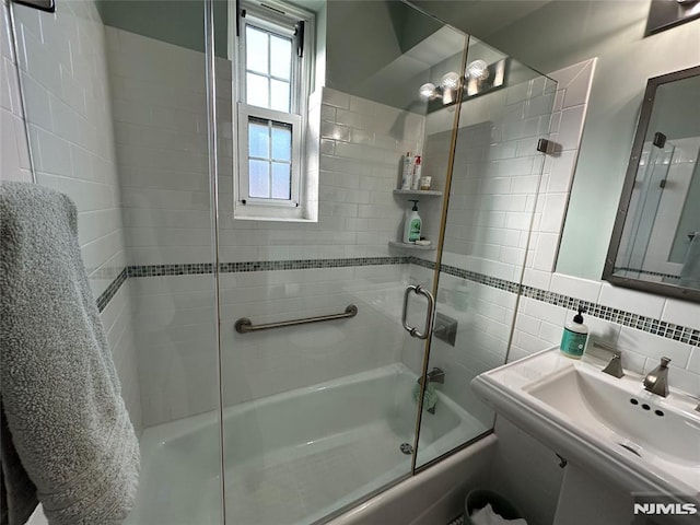 bathroom featuring tasteful backsplash, shower / bath combination with glass door, sink, and tile walls