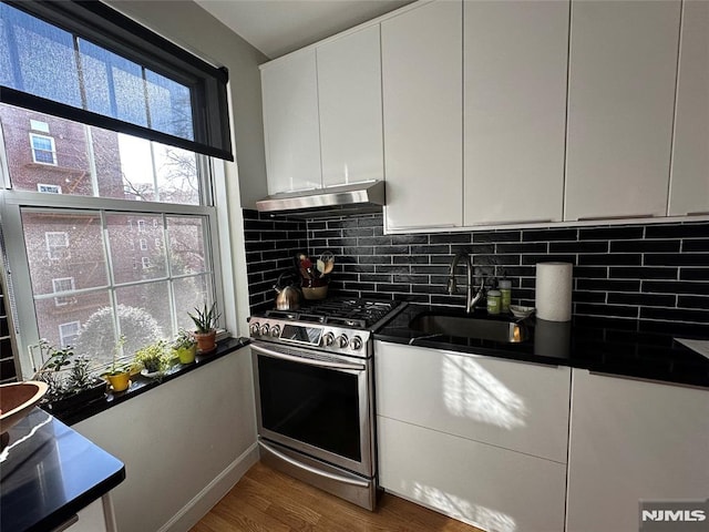 kitchen with hardwood / wood-style floors, white cabinets, sink, stainless steel gas range, and decorative backsplash