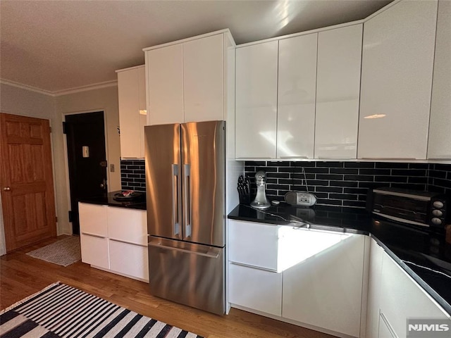 kitchen featuring light wood-type flooring, backsplash, white cabinetry, and stainless steel refrigerator