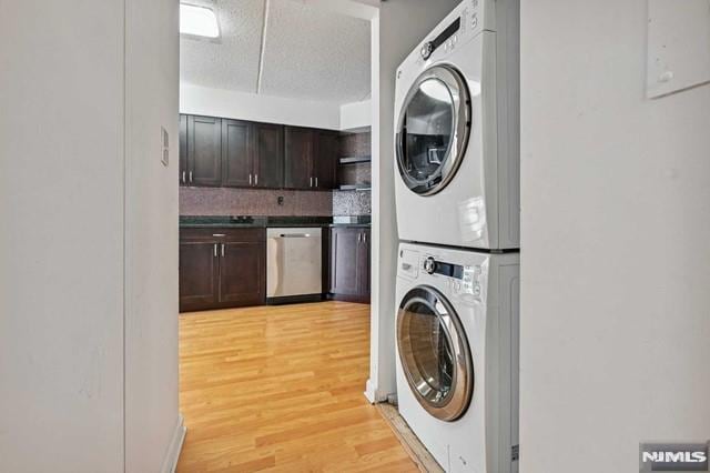 laundry room with a textured ceiling, stacked washing maching and dryer, and light hardwood / wood-style flooring