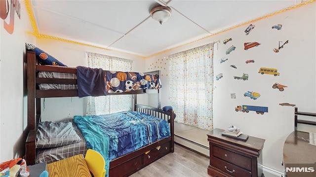 bedroom with a paneled ceiling, light wood-type flooring, and a baseboard heating unit