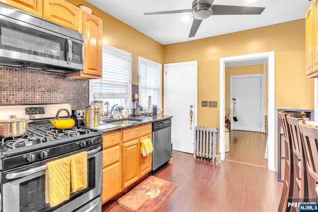 kitchen featuring radiator, sink, tasteful backsplash, light brown cabinetry, and appliances with stainless steel finishes