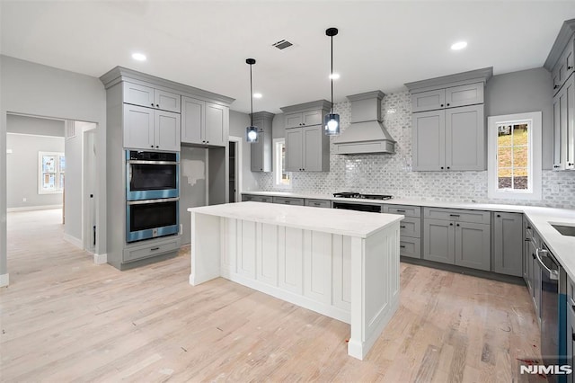 kitchen featuring gray cabinetry, custom exhaust hood, hanging light fixtures, and appliances with stainless steel finishes