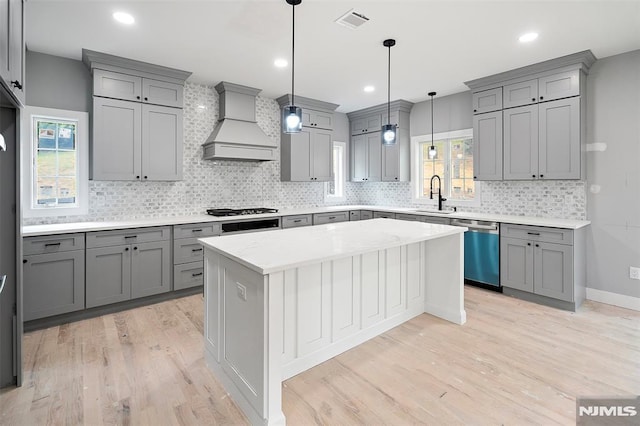 kitchen featuring sink, a center island, premium range hood, gray cabinets, and appliances with stainless steel finishes