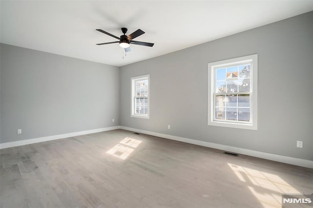 empty room with a wealth of natural light, ceiling fan, and hardwood / wood-style flooring