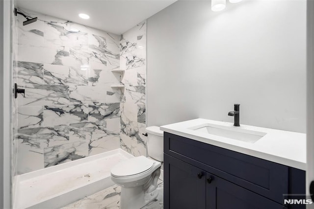 bathroom featuring a tile shower, vanity, and toilet