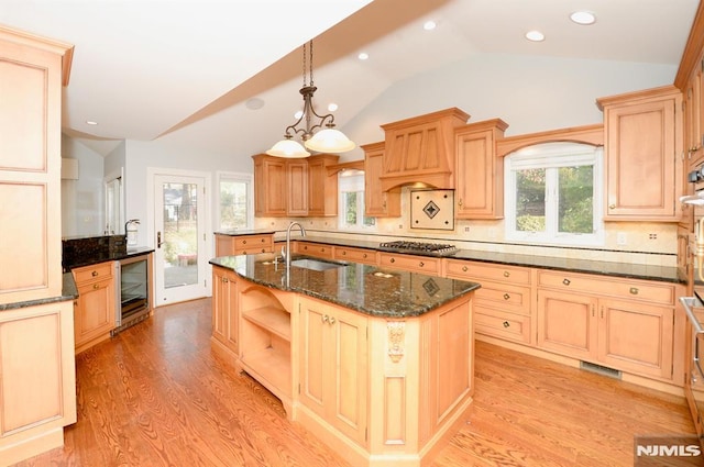 kitchen featuring a kitchen island with sink, vaulted ceiling, light wood-type flooring, sink, and backsplash