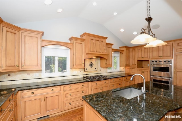 kitchen with dark stone countertops, appliances with stainless steel finishes, hanging light fixtures, sink, and lofted ceiling