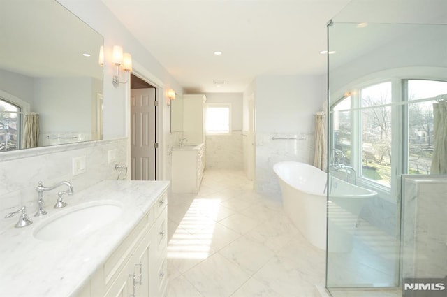 bathroom featuring tile walls, a tub to relax in, and vanity