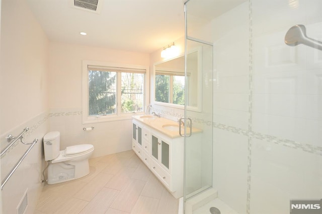 bathroom featuring tile patterned flooring, toilet, vanity, tile walls, and an enclosed shower