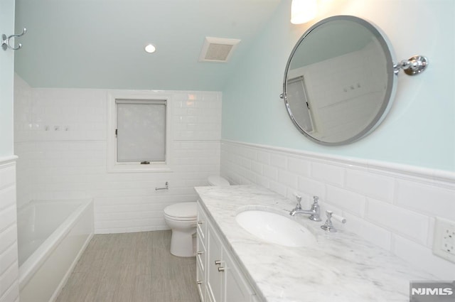 bathroom featuring lofted ceiling, hardwood / wood-style flooring, toilet, a washtub, and vanity