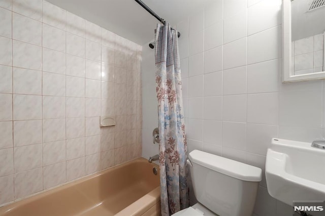 bathroom featuring shower / bathtub combination with curtain, toilet, and tile walls