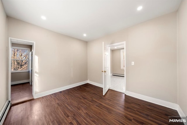 spare room with baseboard heating and dark hardwood / wood-style floors