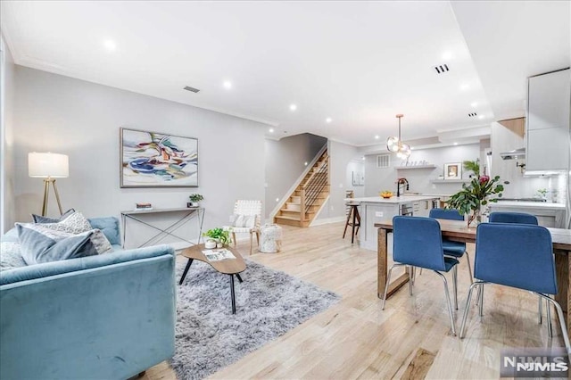 living room with crown molding, light wood-type flooring, and sink