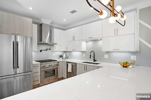 kitchen with light stone countertops, sink, hanging light fixtures, stainless steel appliances, and wall chimney range hood