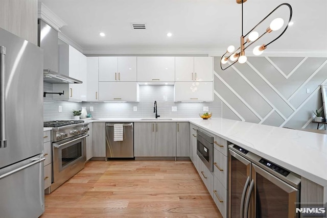 kitchen with sink, wall chimney exhaust hood, hanging light fixtures, stainless steel appliances, and white cabinets