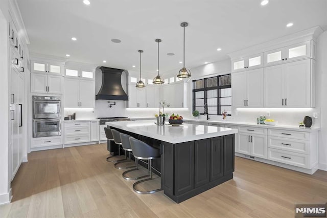 kitchen with stainless steel double oven, a center island, white cabinetry, and custom exhaust hood