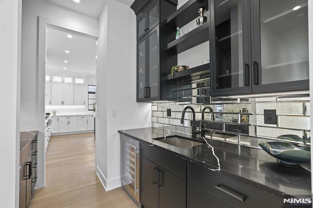 kitchen with sink, wine cooler, dark stone counters, decorative backsplash, and light wood-type flooring