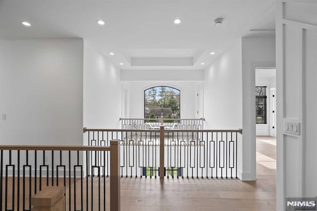 hallway with light wood-type flooring and a raised ceiling