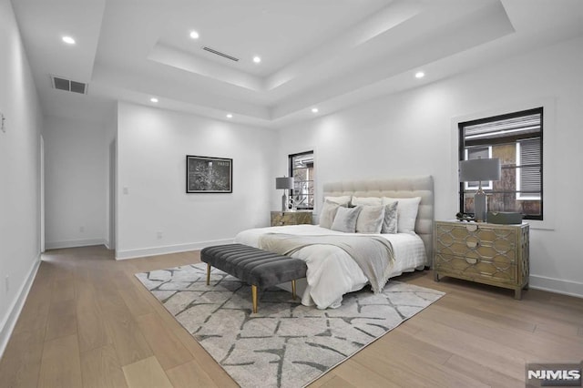 bedroom with light wood-type flooring, multiple windows, and a tray ceiling