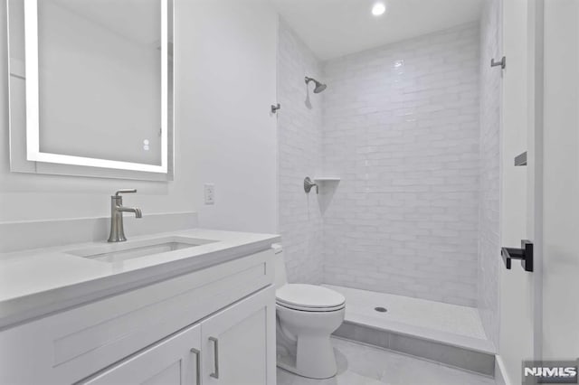 bathroom featuring tile patterned flooring, vanity, toilet, and a tile shower