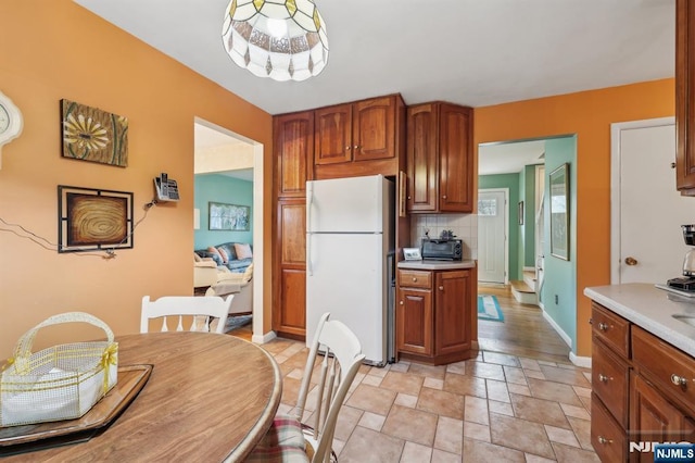 kitchen featuring tasteful backsplash, baseboards, brown cabinets, freestanding refrigerator, and light countertops