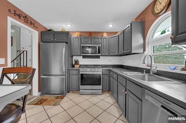 kitchen with gray cabinetry, sink, light tile patterned floors, and appliances with stainless steel finishes