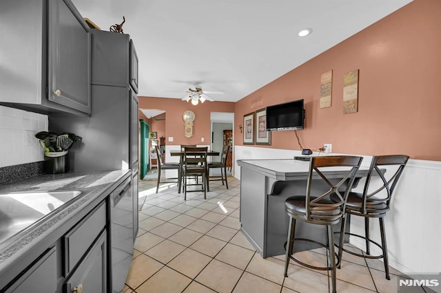 kitchen with stainless steel dishwasher, gray cabinetry, a breakfast bar, ceiling fan, and light tile patterned floors