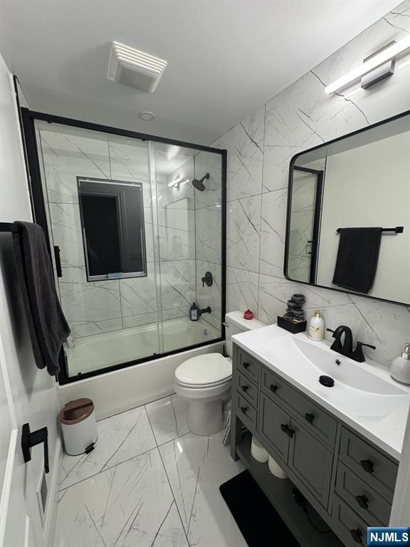 full bathroom featuring combined bath / shower with glass door, tile walls, vanity, tasteful backsplash, and toilet