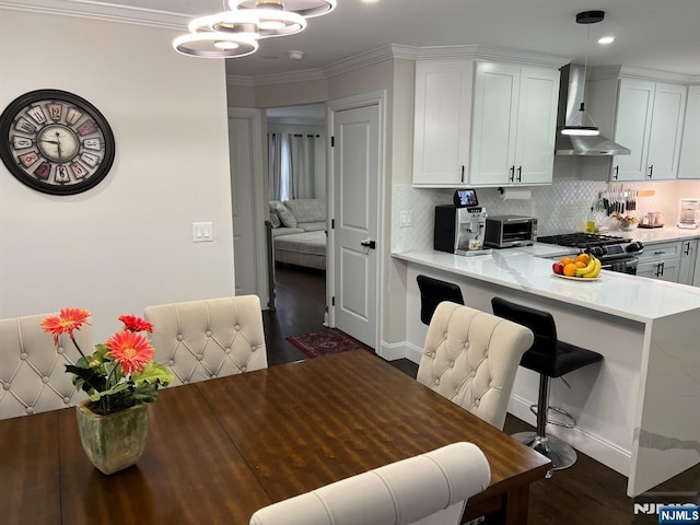 kitchen featuring dark hardwood / wood-style floors, range with gas stovetop, pendant lighting, wall chimney range hood, and white cabinets